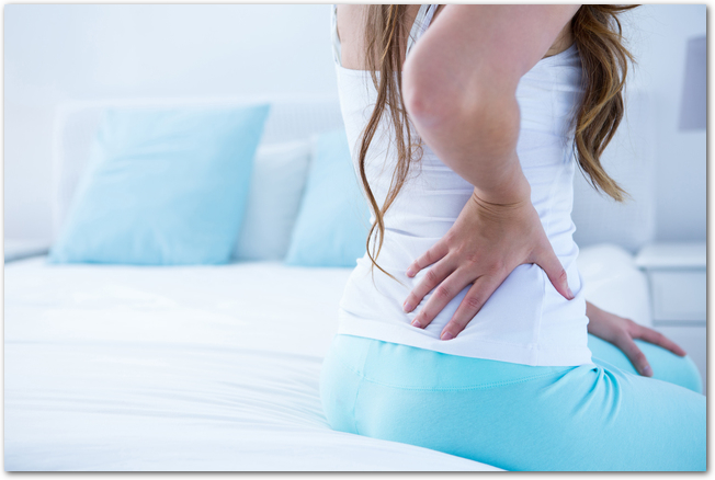Attractive woman with back pain at home in the bedroom